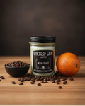 Wicked Lion candle with coffee beans and an orange on a wooden surface