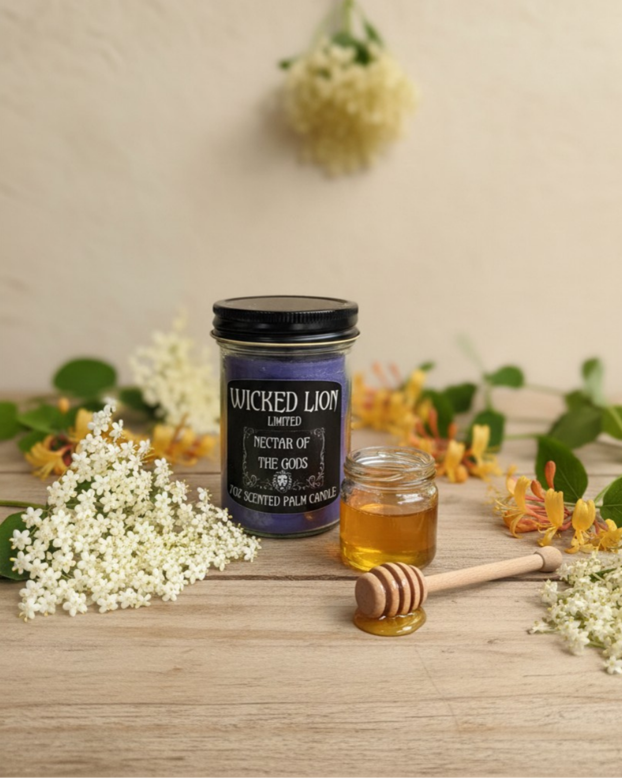 Wicked Lion candle and honey jar with a wooden dipper on a wooden surface with flowers and leaves.